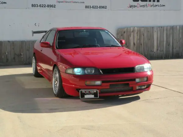 Red Japanese coupe parked in front of a fence.