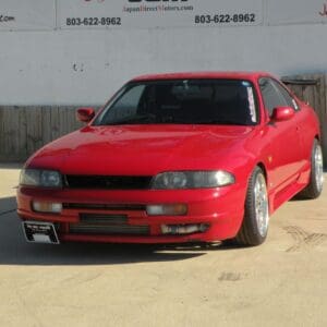 Red Nissan Skyline R33 parked outside.