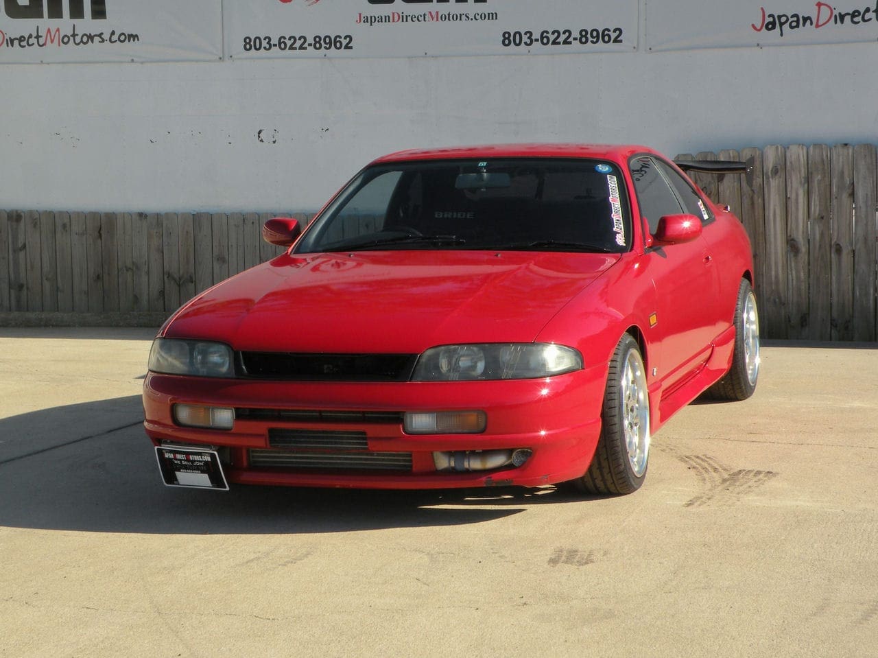 Red Nissan Skyline R33 parked outside.