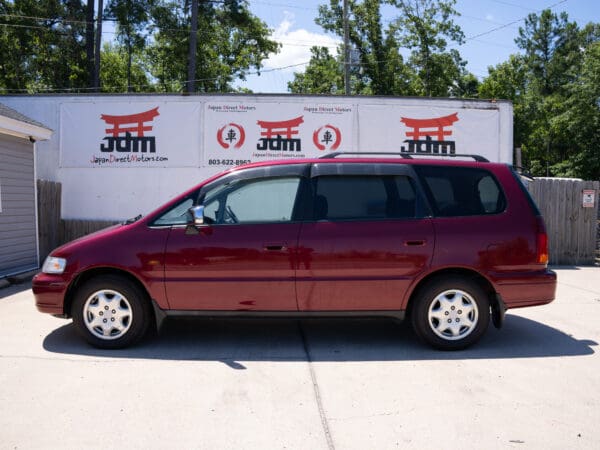 Red Honda minivan parked in front of a sign.