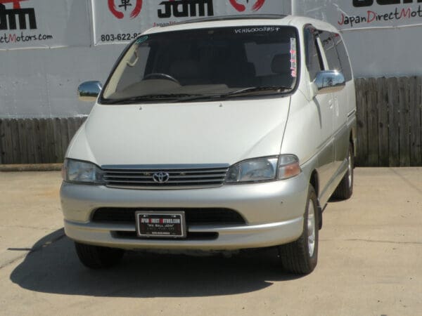 White Toyota minivan parked in front of a fence.