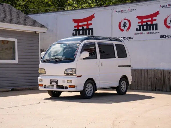 White Japanese van parked in front of a dealership.