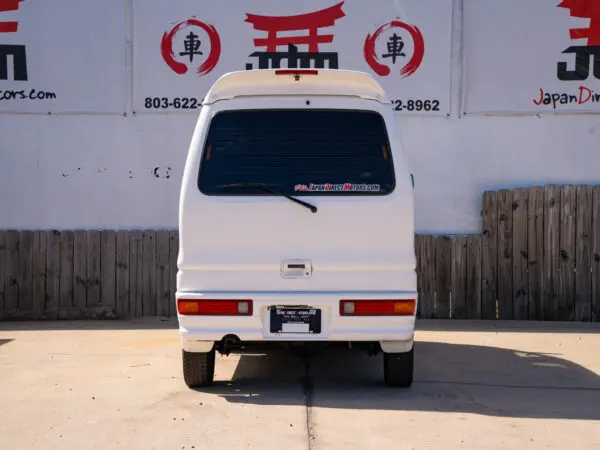 White van parked in front of a fence.