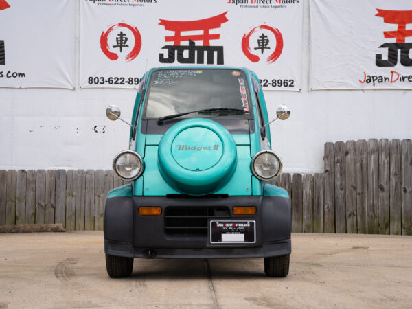 Teal Midget II car in front of a building.