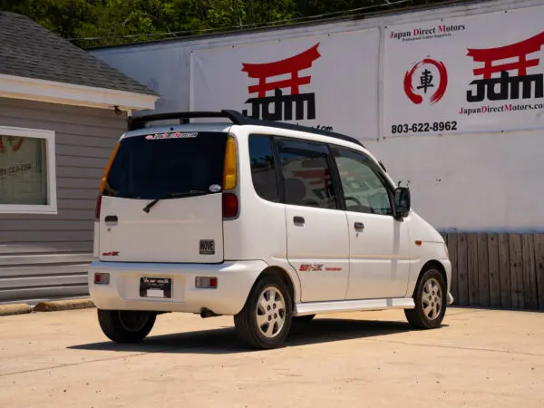 White Daihatsu Move parked in front of a dealership.