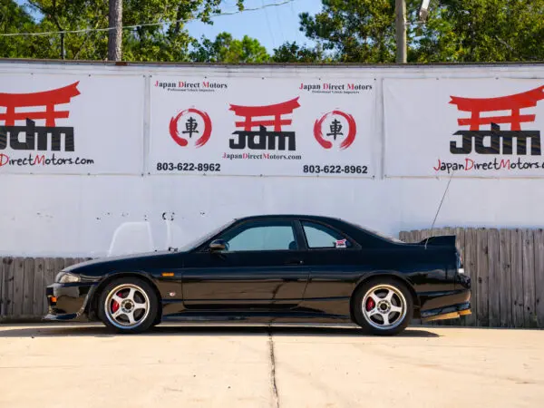 Black Nissan Skyline R33 parked in front of a sign.