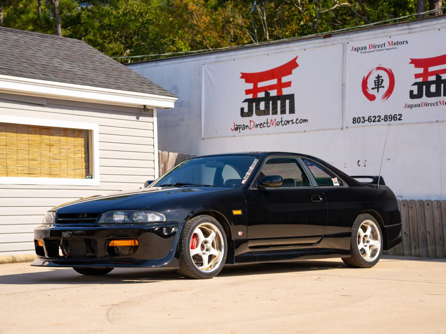 Black Nissan Skyline R33 parked in front of building.