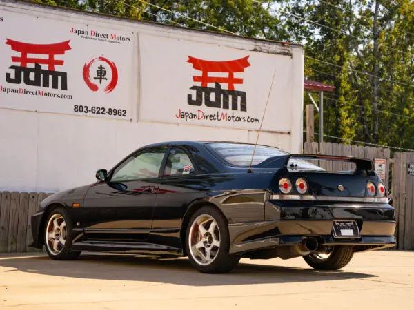 Black Nissan Skyline R33 parked in front of a sign.