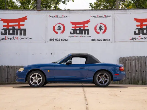 Blue convertible Mazda Miata in front of a sign.