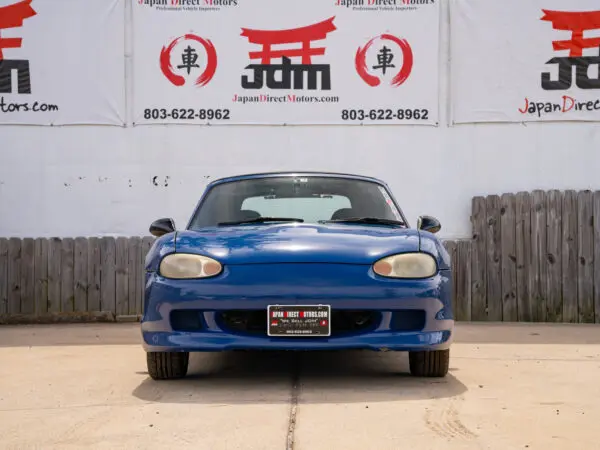 Blue Mazda Miata parked in front of building.