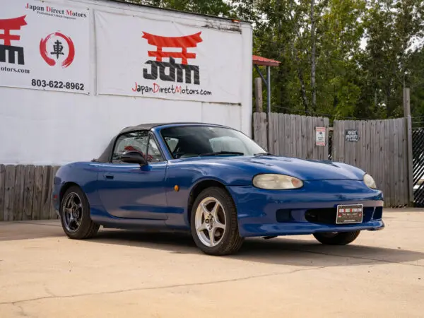 Blue convertible Mazda Miata parked outside.