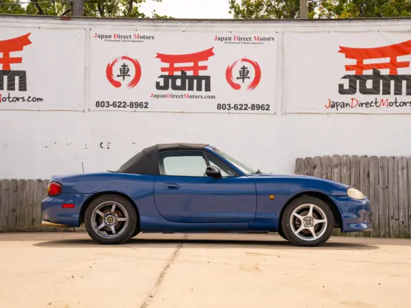 Blue convertible Mazda Miata parked by a sign.