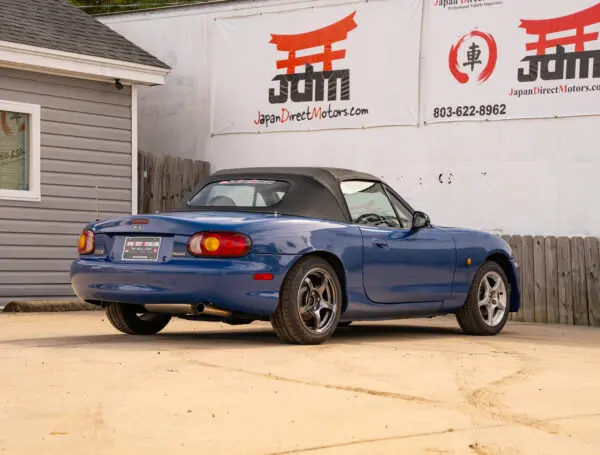 Blue convertible Mazda Miata parked on sand.