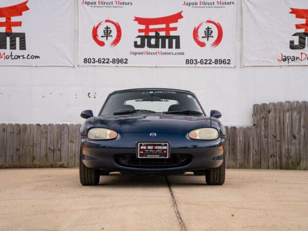 Blue Mazda Miata in front of a building.