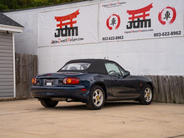 Blue convertible Mazda Miata parked by JDM sign.